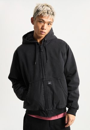 Zwarte zip-up hoodie met een kangoeroezak en een capuchon met trekkoord. Gemaakt van zachte stof met geribbelde boorden en zoom; heeft een logolabel op de zak.