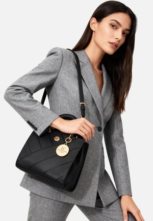 Borsa strutturata nera con cuciture diagonali, dettagli in oro e un ciondolo rotondo. La borsa presenta una maniglia superiore e una tracolla staccabile.