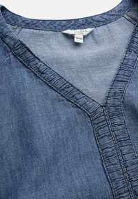 Sininen denimvaate, jonka kaula-aukossa on röyhelöreunus ja ommeltu etiketti, jossa lukee "Cellbes of Sweden" koossa 38/40.
