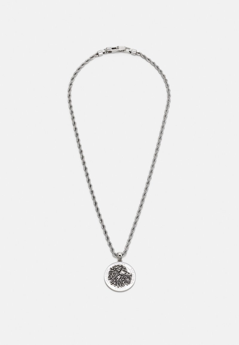 Collier chaîne en argent avec un pendentif rond présentant une tête de lion détaillée et le nom de la marque gravé autour du bord sur un fond blanc.