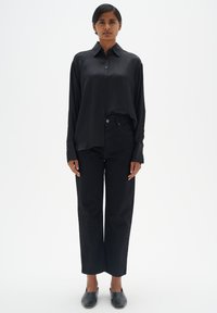 Schwarzes Satin-Hemd mit Knöpfen, entspannter Schnitt mit langen Ärmeln und Manschetten. Kombiniert mit hoch taillierten schwarzenweiten Jeans und eleganten schwarzen Schuhen.