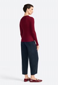 Pull rouge côtelé à manches longues, associé à un pantalon noir ample. Des ballerines bordeaux brillantes complètent la tenue.