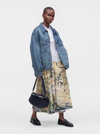 Femme portant une veste en jean oversize, une jupe midi à motifs, une chemise blanche à col, des mocassins noirs, et tenant un sac à main bleu marine.