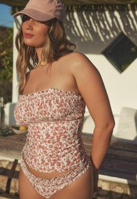 Bikini top bez ramínek s květinovým potiskem v růžové a bílé barvě, s nařasenou texturou. Odpovídající kalhotky se stejným designem a nařasenými detaily.