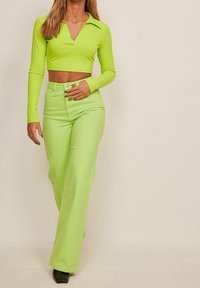 Limettengrünes, geripptes Cropped-Top mit kragenloser Halslinie, kombiniert mit passenden, hochgeschnittenen, weiten Hosen. Glatte Textur, taillierte Passform.