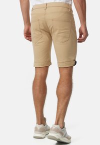 Beige bomullsshorts med rullade fållar, med dubbel bakficka och en smal passform, matchade med ljusa sneakers.