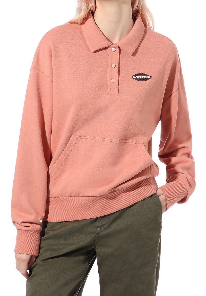 Helles rosa Sweatshirt mit kragenartigem Ausschnitt, drei Knöpfen, einer Brusttasche und einem Vans-Logo-Patch. Der Stoff wirkt weich und leicht strukturiert.