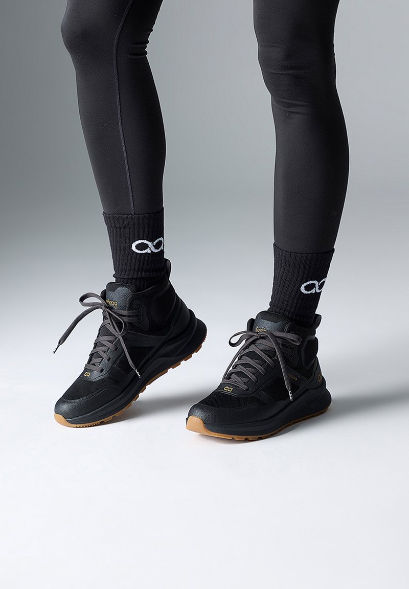 Des chaussures de sport noires avec une semelle en caoutchouc, dotées de panneaux en maille et d'une semelle épaisse. Associées à des chaussettes côtelées noires affichant un logo.