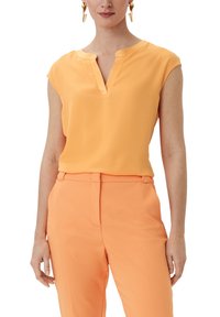 Ærmeløs orange bluse med V-hals og blødt stof. Kombineret med matchende orange skræddersyede bukser, hvilket skaber et sammenhængende look.