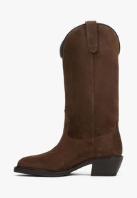 Hnědá semišová kovbojská bota s špičatou špicí, výškou do poloviny lýtek a s vysokým podpatkem. Disponuje poutkem na vrchu pro snadné obouvání.