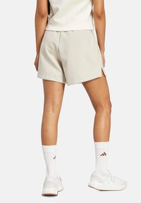 Beige šortky vyrobené z měkkého materiálu s volným střihem a postranními rozparky, doplněné bílými ponožkami a bílými teniskami s jemnými akcenty.