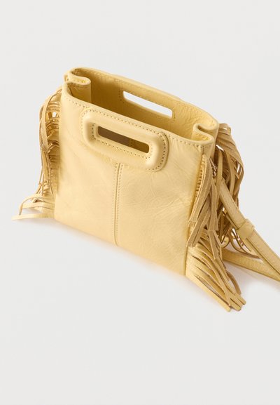Κίτρινη δερμάτινη τσάντα με λαβές με ανοίγματα και μακριές φούντες στα πλάγια, εμφανίζεται σε λευκό φόντο.