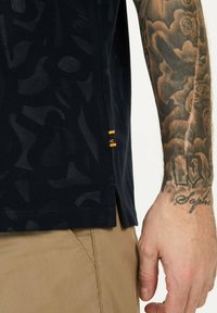 Donkerblauwe shirt met korte mouwen met een abstract patroon, gemaakt van gestructureerde stof, met zijsplitten en oranje accentdetails.