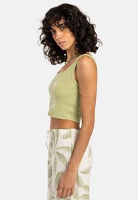 Light green ribbed crop tank top with a rounded neckline. Paired with cream pants featuring green palm leaf patterns and an elastic waistband.