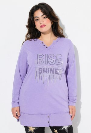 Langärmliges, locker sitzendes lilafarbenes Oberteil mit V-Ausschnitt und drei dekorativen Knöpfen. Besitzt ein glitzerndes "RISE SHINE"-Grafikdesign mit Sternakzenten.