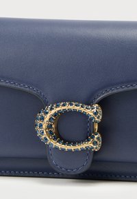 Marineblauwe leren portemonnee met gegraveerde gouden accessoires en blauwe edelstenen. Gladde textuur met contrasterende stikseldetails. Compacte rechthoekige vorm.