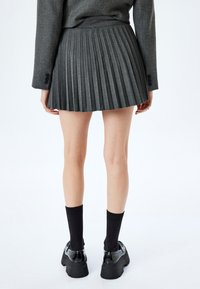 Grijze geplooide rok van textiel, tot halverwege de dij, gecombineerd met zwarte geribde sokken en stevige zwarte schoenen.