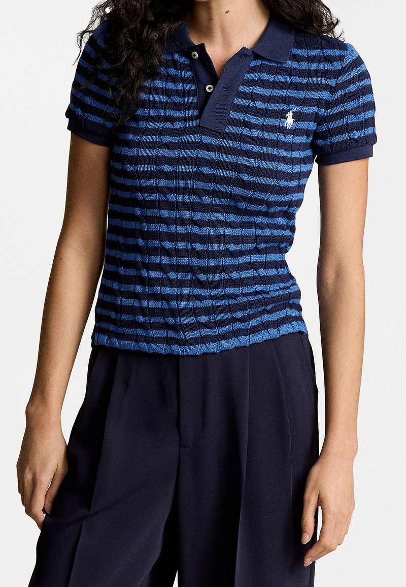 Mujer vistiendo una camiseta de punto ajustada en azul marino y azul a rayas, con cuello y mangas cortas, combinada con pantalones holgados en azul marino.