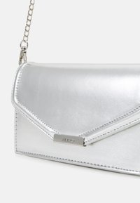 Srebrna metaliczna kopertówka z klapą z zakładką, przeszyciami oraz metalową plakietką z logo ALDO. Posiada srebrny łańcuszkowy pasek do noszenia.