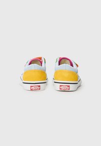 Baskets Vans avec un mélange de daim bleu, un talon jaune et des accents colorés. Semelle en caoutchouc blanc avec une bordure noire et un logo sur le talon.
