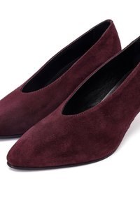 Zapatos de ante burdeos con punta afilada y diseño cortado, con interior negro. La textura suave y la forma estilizada destacan el estilo minimalista.