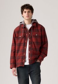 Red and black plaid shirt jacket with grey hooded lining, snap buttons, two chest pockets, and a relaxed fit. Cotton blend material.