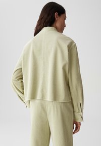 Giacca in corduroy verde chiaro con vestibilità morbida, caratterizzata da colletto, polsini e una superficie testurizzata. Abbinata a pantaloni coordinati, che mettono in evidenza la semplicità.