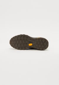 Vibram sole with textured pattern in dark brown, featuring grooves and chevron shapes for traction; bright yellow logo detail.