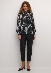 Zwart-witte geplooide blouse met een hoge hals en lange mouwen, gecombineerd met zwarte leren tapered broeken en puntige hakken.