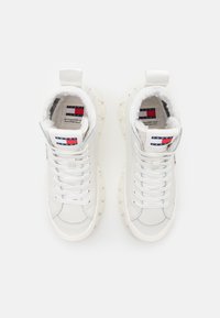 Białe sneakersy za kostkę z teksturowaną powierzchnią, z wyściełanym kołnierzem, sześciokątną podeszwą i markową metką na języku.
