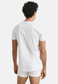 Hvid bomulds T-shirt med korte ærmer, rund hals og en afslappet pasform. Båret med hvide underbukser, vist bagfra. Glat tekstur.