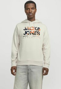 Sudadera crema hecha de tela suave; presenta un gráfico central con "JACK & JONES" en negro y naranja. Capucha ajustable y puños de canalé.