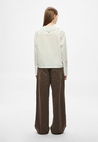 Koszula w paski w jasnym kolorze z falbanianym kołnierzem, zestawiona z wysokim stanem i szerokimi nogawkami w brązowym kolorze, wyposażonymi w tylne kieszenie.