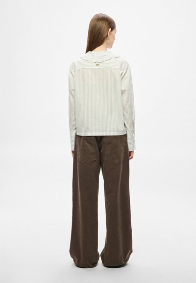 Chemise rayée de couleur claire avec un col à volants, associée à un pantalon marron taille haute à jambes larges avec des poches arrière.