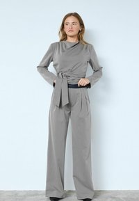 Szürke, szabott öltöny, amely idomított felsőrészt tartalmaz lehulló nyakkivágással és megkötött derékkal, magas derekú, bő szárú nadrággal párosítva.