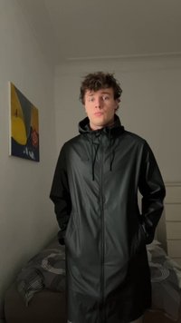 Svart vanntett jakke med hette, frontlomme og sidelommer. Glatt tekstur og lett skinnende overflate. Lang, løs passform.