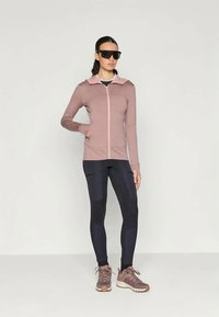 Felpa rosa con zip e dettagli chiari, abbinata a leggins navy scuri. Scarpe sportive marroni con suola chiara, modello che indossa occhiali da sole.