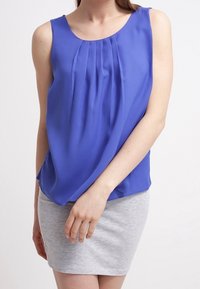 Sininen hihaton paita, jossa on laskostettu etuosan yksityiskohta, yhdistetty vaaleanharmaaseen istuvaan hameeseen. Sileä kangaspinta, rento istuvuus.