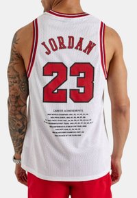 Hvid basketballtrøje med røde detaljer, der har "JORDAN" og "23" i fed rød skrift, mesh tekstur og en liste over karrierepræstationer på ryggen.
