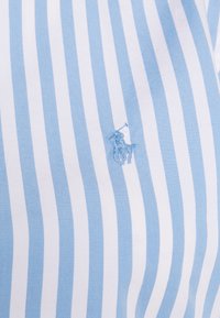 Ljust blåvitrandig skjorta i bomull, med en broderad logotyp av en häst med ryttare p å vänster sida.