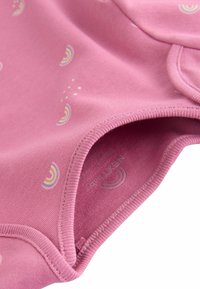 Combinaison en coton rose ornée de petits motifs arc-en-ciel colorés. Encolure arrondie, manches courtes et fermetures à pression au bas.
