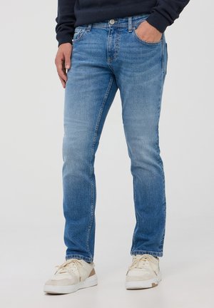 Jeans in denim blu con una vestibilità slim, lavaggio chiaro e dettagli sbiaditi; indossati con sneakers bianche. Presentano due tasche frontali e chiusura con bottone.