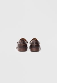 Par de zapatos de vestir de cuero marrón mostrados por la parte de atrás sobre un fondo blanco con tacones de madera y detalles de costura visibles.