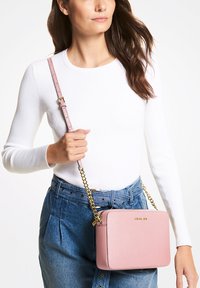 Lyserød læder crossbody taske med en guld kædedyse, rektangulær form, glat tekstur og en subtil brandingdetalje på fronten.