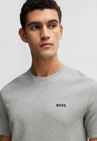 Graues, strukturiertes T-Shirt mit rundem Halsausschnitt und kurzen Ärmeln. Verfügt über ein schwarzes "BOSS"-Logo auf der Brust. Einfaches und modernes Design.