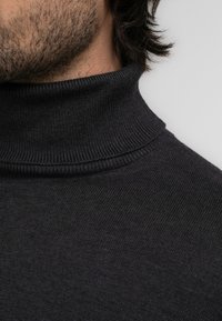 Ciemnoszary sweter z golfem o teksturze ryżu. Kołnierz jest dopasowany i wysoki, co zapewnia płynne przejście do korpusu.