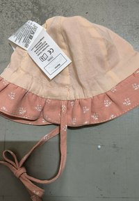 Cappello a secchiello in cotone rosa e pesca con ricamo floreale, bordo arricciato e legaccio regolabile. Etichetta di cura attaccata all'interno.