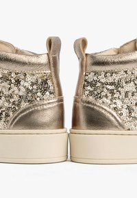 Gold-glänzende Ankle Boots mit einer schimmernden Metalloberfläche und einem strukturierten Absatz. Sie verfügen über eine leichte weiße Sohle und Zuglaschen für ein einfaches Anziehen.