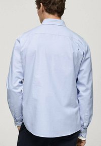Chemise à manches longues bleu clair avec un col classique ; fabriquée en tissu de coton lisse ; possède des poignets boutonnés et un ourlet arrondi.