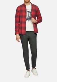 Rood geruite overhemdo over een wit graphic t-shirt, gecombineerd met donkere slim-fit broek en witte sneakers.